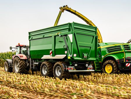 Landwirtschaftlicher Muldenkipper wird beim Häckseln von Mais auf dem Feld beladen