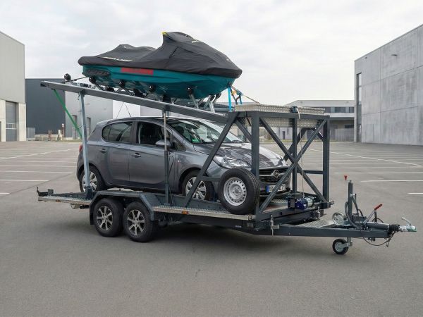 Zweiachsiger Spezialanhänger für den gleichzeitigen Transport von Auto und Jetski vor modernem Industriehintergrund.