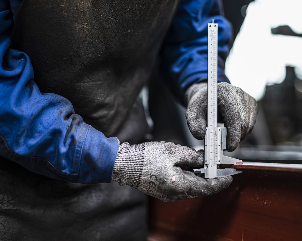Mitarbeiter im Fahrzeugbau misst ein Metallbauteil mit Messschieber in der Anhängerfertigung