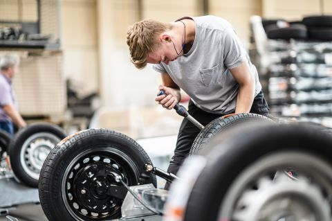 Ein junger Mechaniker montiert Reifen mit Schlagschrauber an einem Anhänger