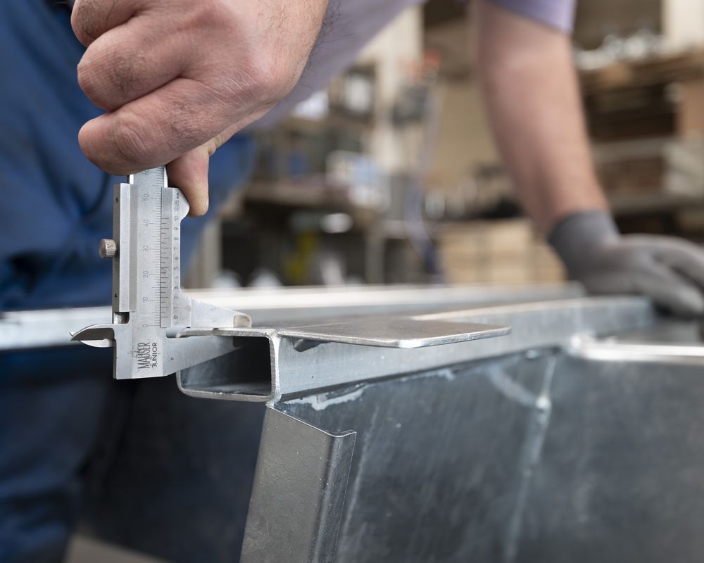 Mitarbeiter im Fahrzeugbau misst ein Metallbauteil mit Messschieber in der Anhängerfertigung