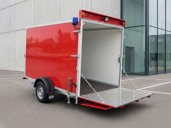 Roter Kofferanhänger mit geöffneter Auffahrrampe und blauer Warnleuchte vor einem modernen Industriegebäude