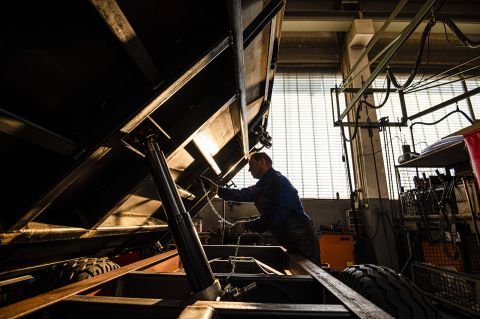 Ein Handwerker montiert und prüft die Kippmechanik und Hydraulik an einem Kippanhänger