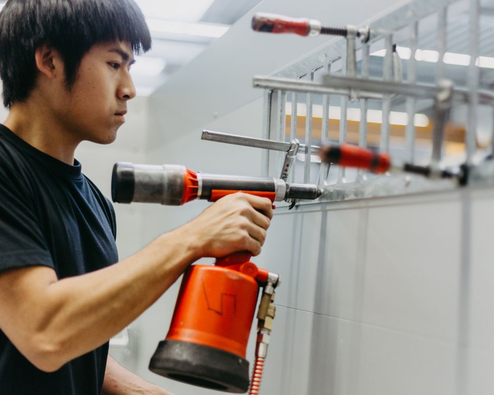 Mitarbeiter im Fahrzeug- und Anhängerbau befestigt mit Druckluftnietgerät ein Bauteil am Aufbau