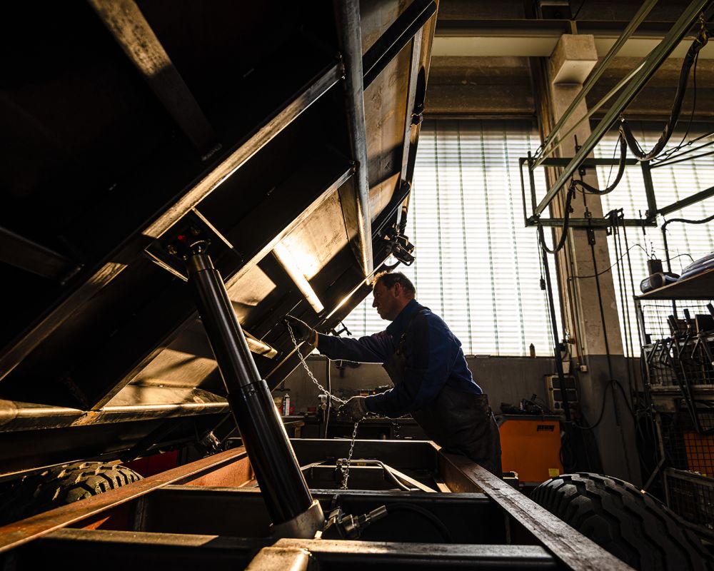 Ein Handwerker montiert und prüft die Kippmechanik und Hydraulik an einem Kippanhänger