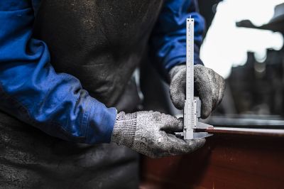 Mitarbeiter im Fahrzeugbau misst ein Metallbauteil mit Messschieber in der Anhängerfertigung