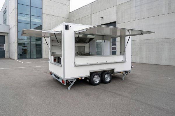 Weißer Küchen-Verkaufsanhänger mit aufgeklappten Klappen und Küchenausstattung auf einem Parkplatz