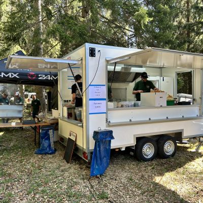 Weißer Verkaufsanhänger mit aufgeklappten Klappen beim Outdoor-Event im Wald