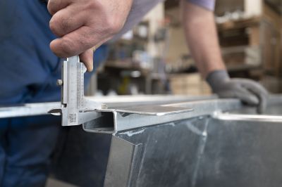 Mitarbeiter im Fahrzeugbau misst ein Metallbauteil mit Messschieber in der Anhängerfertigung