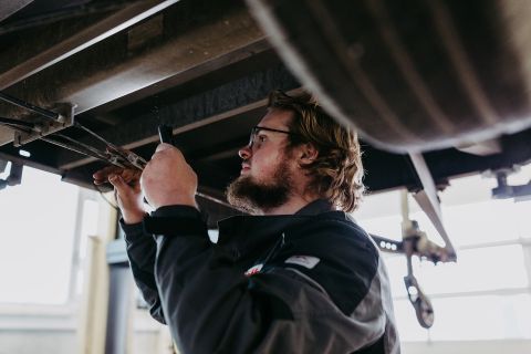Ein Handwerker prüft Bauteile am Fahrgestell eines Anhängers in der Werkstatt
